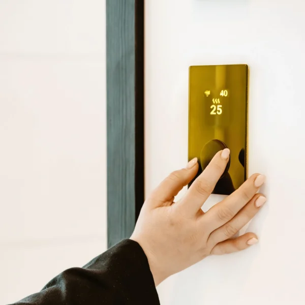 Hand adjusting the HUUM Local Gold control panel on a wall, displaying a temperature of 25°C.