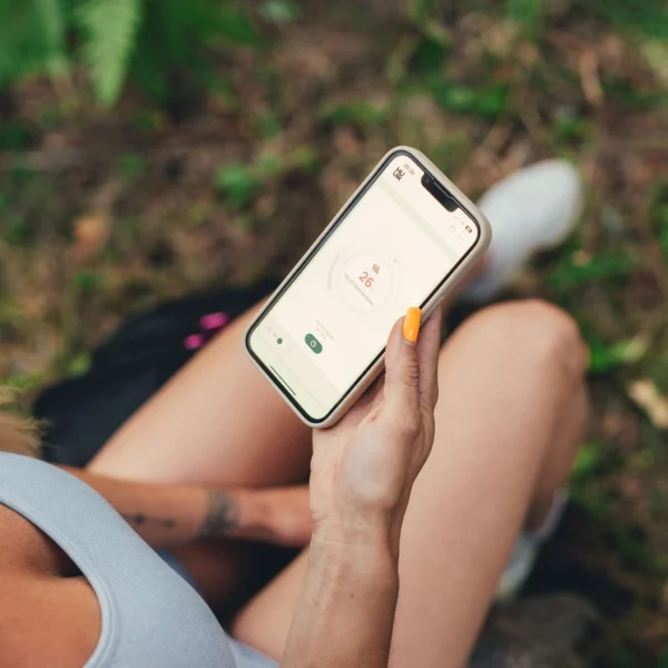 Person holding a smartphone outdoors, displaying the HUUM app with temperature controls set at 26°C.