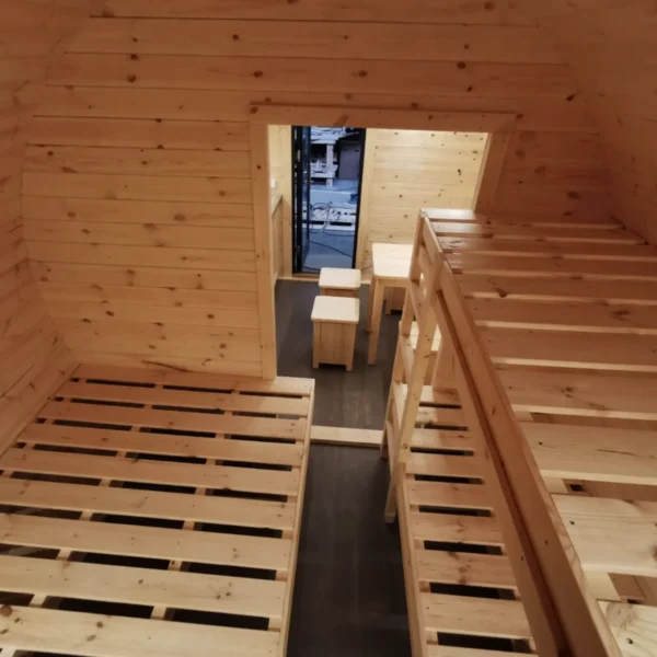 Interior of a 3x4.8m wooden camping barrel featuring bunk bed frames, wooden walls, and a cozy layout for group accommodations.