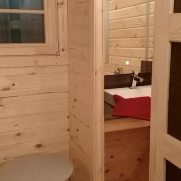 Interior of a 3x4.8m wooden camping barrel featuring a compact bathroom with a toilet and sink, designed for convenience.