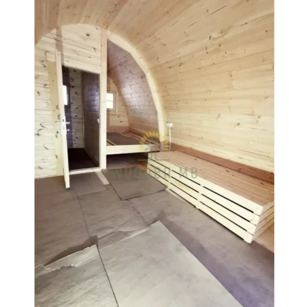 Interior of a wooden camping pod with benches, arched ceiling, and separate room, ideal for cozy outdoor accommodations.