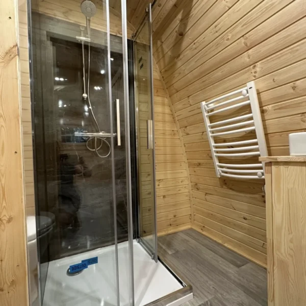 Interior of an insulated camping pod featuring a modern shower, wooden walls, and a heated towel rack for added comfort.