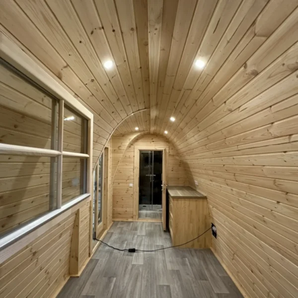 Spacious interior of an insulated camping pod with wooden walls, arched ceiling, built-in lighting, and a modern finish.