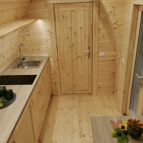Interior of an insulated camping pod with a small kitchen, wooden walls, and a cozy design, perfect for outdoor living.