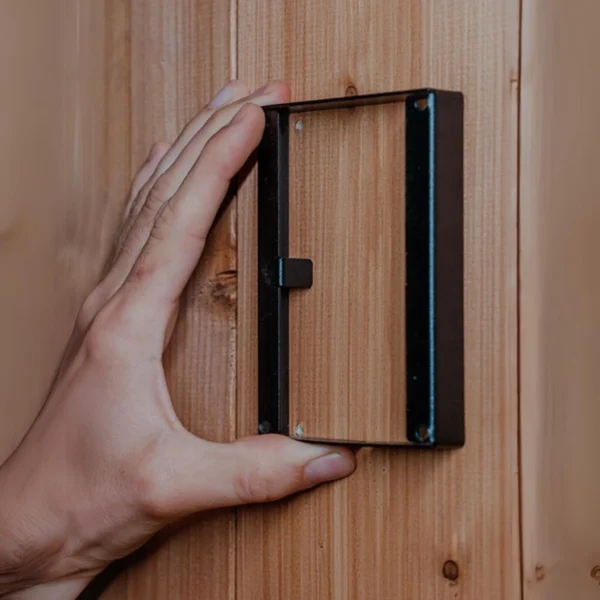 Installation of HUUM UKU Surface Mounting Frame on a wooden sauna wall.
