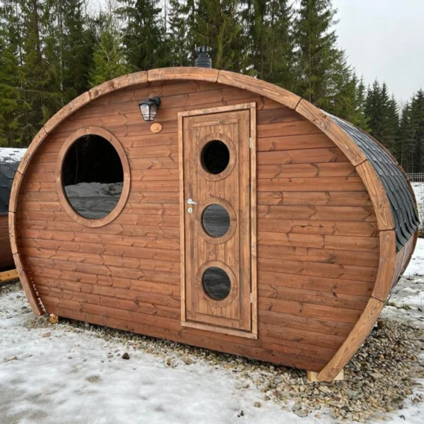 Close-up of the Ilmarinen sauna’s finished wooden exterior, featuring a modern design with a round window, three-pane door, and robust materials for long-lasting outdoor use in any weather.