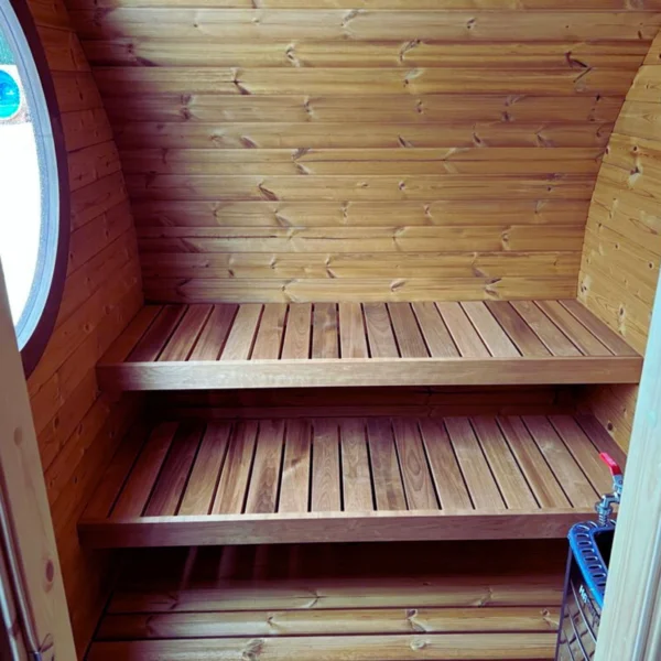 Interior view of the Ilmarinen sauna benches, highlighting the finely crafted wooden slats, double-tier seating arrangement, and a glimpse of the stove to provide a complete and authentic sauna experience.