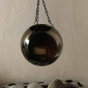 Shiny black sauna aroma ball hanging above sauna stones, designed for enhancing sauna experience with essential oils.