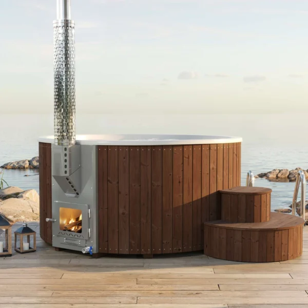 Yoshino Kumano hot tub with brown wooden exterior, silver marine-grade aluminum heater with glass door, installed on a wooden deck with sea view. Designed for comfortable year-round use.