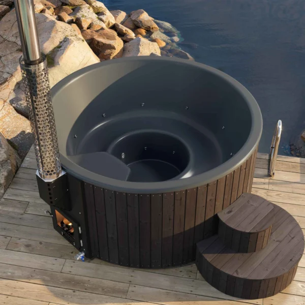 Yoshino Kumano hot tub's dark gray fiberglass interior, ergonomically designed seating for four to five people, marine aluminum heater and chimney, wooden exterior and steps, installed by the sea.